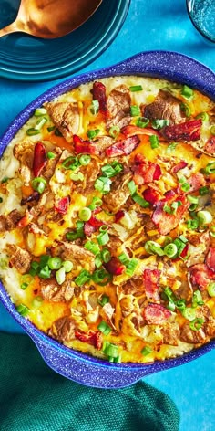 a pizza with meat, cheese and vegetables in a blue dish on a blue table cloth