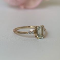 an engagement ring with a large green stone and two small diamonds on the side, sitting next to a pink rose