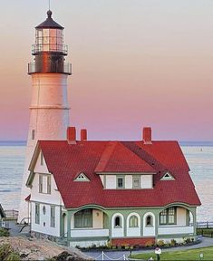 a white and red house sitting on top of a lush green field next to the ocean