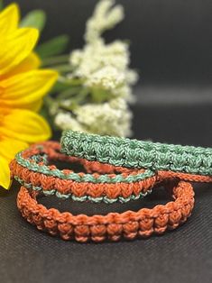 three crocheted bracelets sitting next to a sunflower on a black surface