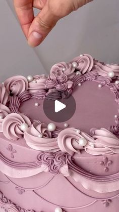 a person is holding a knife over a cake with pink icing and pearls on it