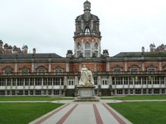 a large building with a statue in front of it on the grass and some buildings behind it