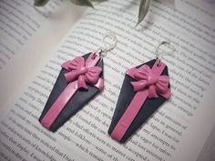 pair of pink and black earrings with bow on them sitting on top of an open book