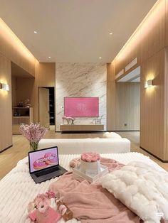 a laptop computer sitting on top of a bed next to pillows and pink flowers in a vase