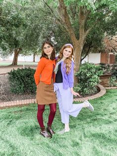 two young women standing next to each other in front of a tree and grass area