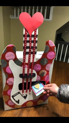 someone is holding their cell phone in front of a guitar shaped box with hearts on it