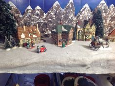 a christmas village is displayed on a table in front of mountains and snow covered trees