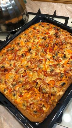 a square pizza sitting on top of a stove next to a pan filled with toppings