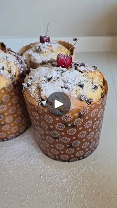 three muffins covered in powdered sugar and cherries on a white counter