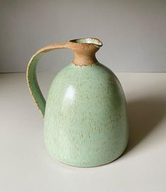 a green ceramic teapot with a wooden handle on a white countertop, in front of a gray background