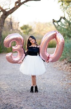 a woman in a tutu and dress holding balloons that spell the number thirty three