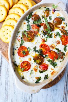 a casserole dish with tomatoes, cheese and spinach in it next to crackers