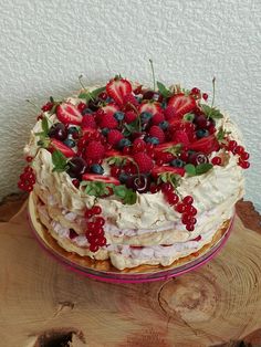 a cake with berries and cream on top is sitting on a tree stump in front of a white wall