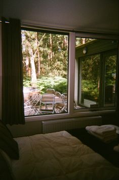 a bed sitting in front of a window next to a wooden table with chairs on it