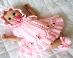 a baby doll laying on top of a bed wearing a pink dress and pacifier