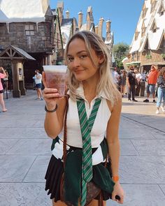 a woman holding a drink in front of a castle at disney world with people walking around