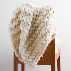 a white blanket sitting on top of a wooden chair in front of a white wall