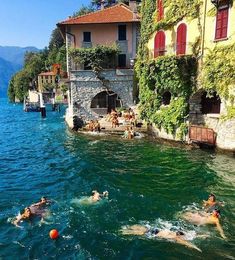 people swimming in the water next to buildings and trees on both sides of the lake