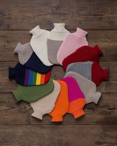 a bunch of sweaters that are on top of a wooden floor, all in different colors