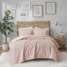 a bed with pink comforter and pillows in a bedroom next to a potted plant