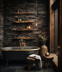 a black and gold bathroom with stone walls, an antique claw foot bathtub and wooden stools