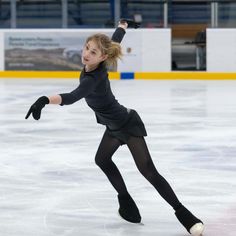 a woman skating on an ice rink wearing black clothing and holding her arms out in the air