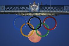 the olympic rings are suspended above the moon in front of an ornate clock on top of a bridge