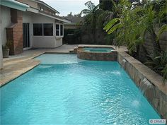 an empty swimming pool in front of a house with palm trees and landscaping around it