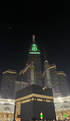 the ka'bah in front of some tall buildings at night with people standing around it