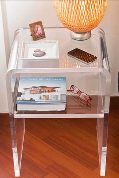 a clear table with some books on top of it and a lamp in the corner