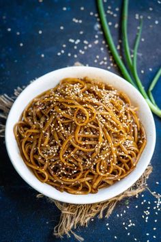 a white bowl filled with noodles and sesame seeds on top of a blue tablecloth