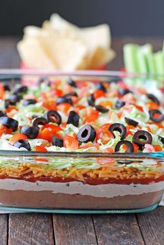 a casserole dish filled with vegetables and olives on a wooden table next to crackers