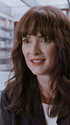 a woman with long brown hair and bangs smiles at the camera while wearing a black jacket