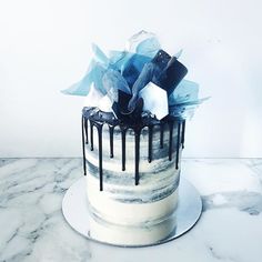 a white cake with black and blue icing on it sitting on a marble table