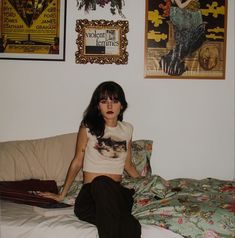 a woman sitting on top of a bed in front of pictures and posters above her head