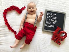 a baby laying on top of a bed next to a love sign and a red heart