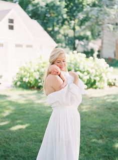 a woman in a white dress holding a baby on her chest and looking at the camera