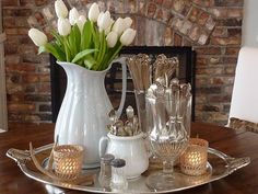 a tray with flowers and glasses on it in front of a fire place, next to a fireplace