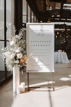 a sign with flowers and candles in front of it on a table at a wedding