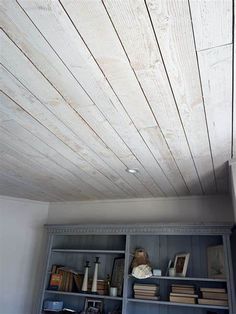 a book shelf with books and other items on it in front of a white painted ceiling