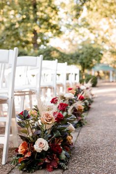 rows of white chairs with red and orange flowers on the ground next to each other