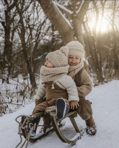 two children are sitting on a sled in the snow, one is holding the other