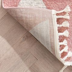 a pink and white rug with tassels on the floor next to a wooden floor