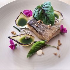 a white plate topped with fish covered in green sauce and flowers on top of it