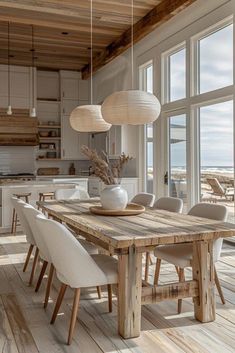 a dining room table with white chairs and an open kitchen area in front of large windows