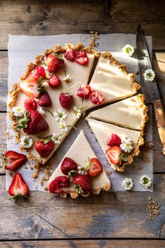 a cheesecake with strawberries on top is cut into slices and sits on a piece of parchment paper