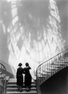 two women are standing on the stairs in front of a wall with shadows coming from it