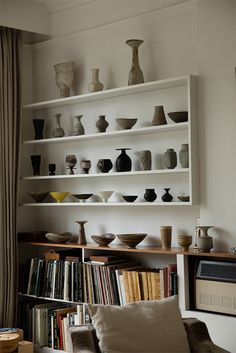 a living room filled with lots of books and vases on top of white shelves