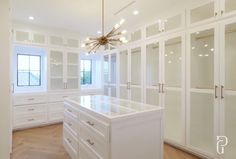 a large white closet with lots of glass doors and drawers on the walls, along with a chandelier hanging from the ceiling