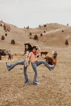 two people are dancing in the middle of a field with cows behind them and one person is holding on to his back